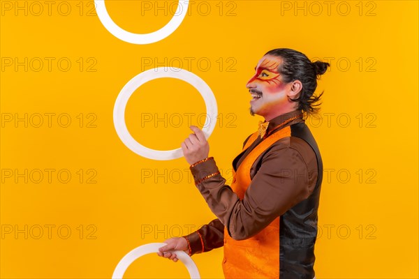 Portrait of a juggler in a vest with a painted face juggling hoops on a yellow background