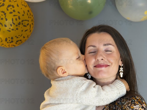 Young pretty mother is kissed on the cheek by her one year old son on his first birthday