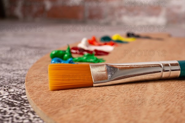 Close-up brush with out-of-focus oil paint colors on a wooden palette