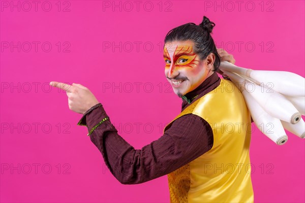 Juggler in a vest and with painted face juggling maces on a pink background