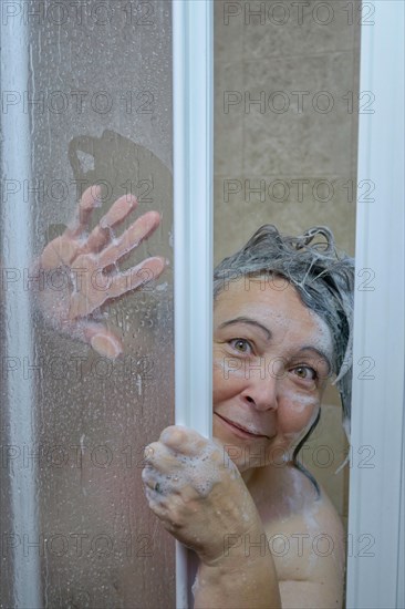 Woman in the shower covered with soap looking at the camera