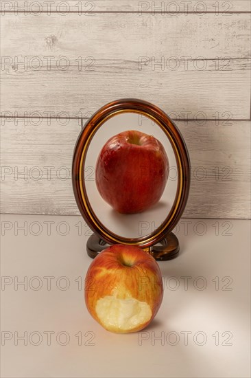 Bitten red apple reflected in a mirror isolated on a white table with copy space