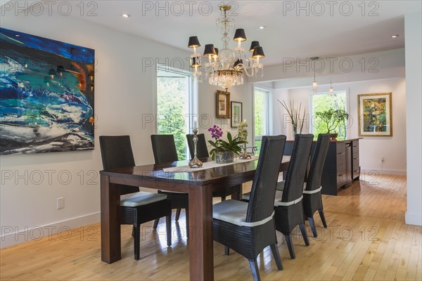 Walnut colored wooden dining table with black high back wicker chairs in dining room inside modern home