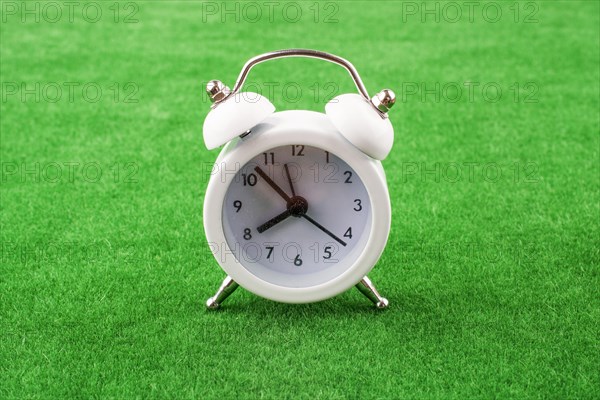 White color alarm clock a on a green grass background