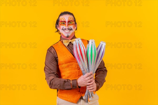 Happy juggler man in makeup vest juggling maces on a yellow background