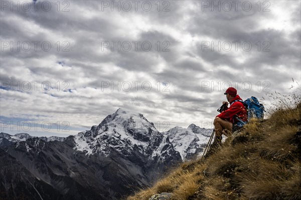 Mountaineer on autumnal mountain meadow with cloudy sky in front of Ortler summit massif