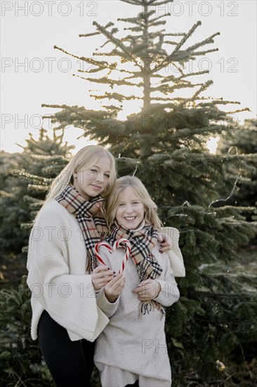 Two girls with candy cane hearts in front of a Christmas tree