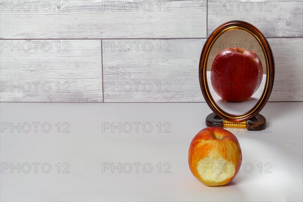 Bitten red apple reflected in a mirror isolated on a white table with copy space