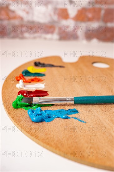 Wooden palette with colored oil paints and brushes isolated on a white background