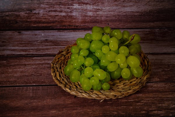 Close-up of a bunch of green grapes on an esparto grass tray with a dark wood background