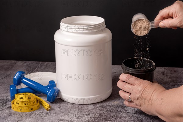 Woman pouring a scoop of protein powder in an insulated shaker on a black background