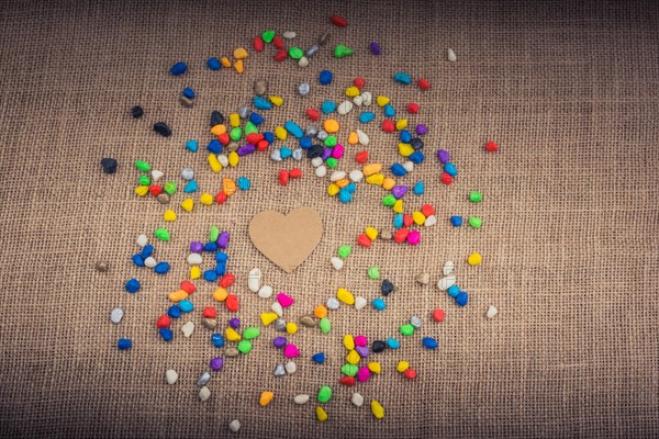 Paper heart amid colorful pebbles on canvas ground