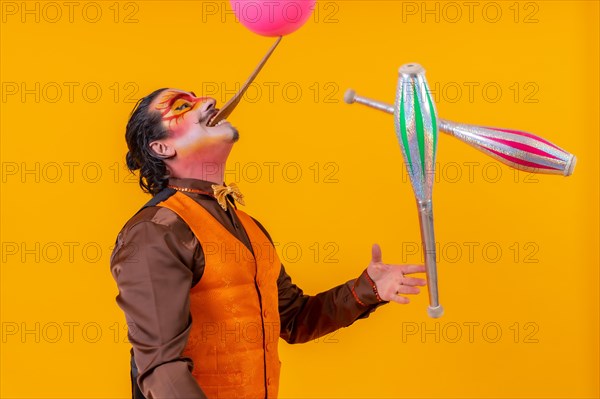 Portrait of a juggler in a vest with a painted face juggling with maces on a yellow background