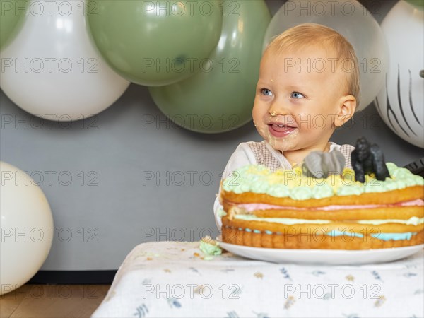 One-year-old boy sits in front of his birthday cake on his first birthday and tries to see if it tastes good