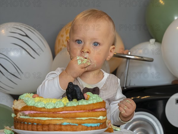 One-year-old boy sits in front of his birthday cake on his first birthday and tries to see if it tastes good