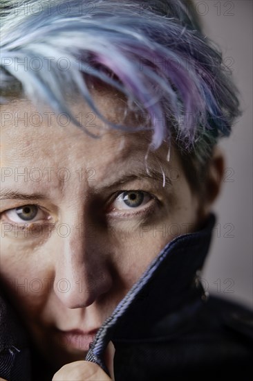 Androgynous woman with dyed hair pulls up the collar of her denim jacket