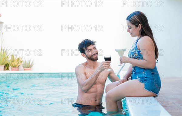 Smiling couple enjoying and toasting in swimming pool. Young man and woman on vacation toasting in the pool