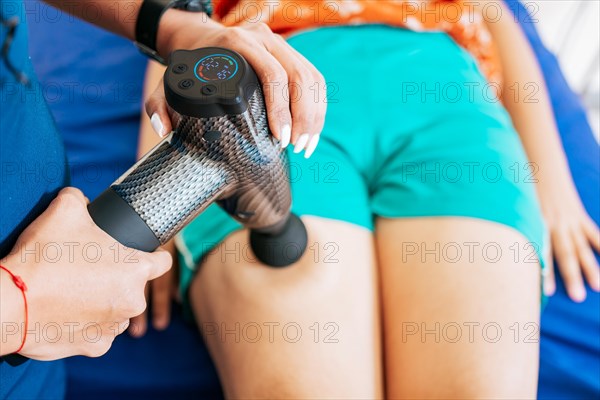 Chiropractor using massage gun on patient leg