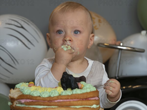 One-year-old boy sits in front of his birthday cake on his first birthday and tries to see if it tastes good