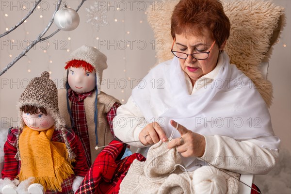 A nice elderly woman sews to knit her granddaughters in a Christmas arrangement. In studio