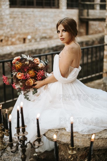 Beautiful bride with her bouquet sittitng in the stone garden with candles