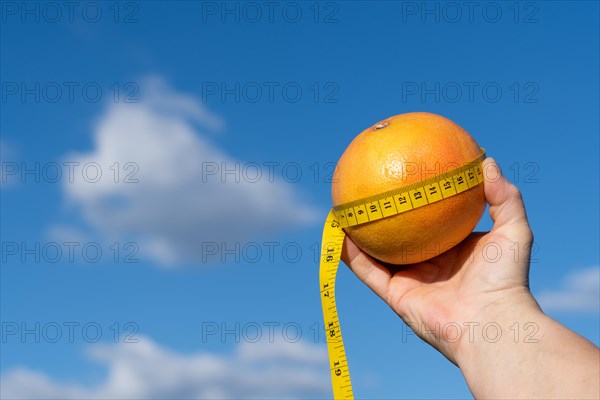 Woman holding a grapefruit in her hands with a tape measure and a sky with clouds in the background