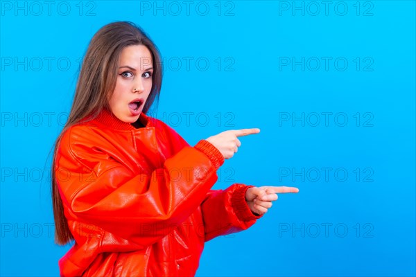 Attractive woman smiling pointing fingers at copy space on blue background