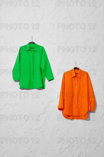 Two bright green and orange shirts on hanger hang on white wall