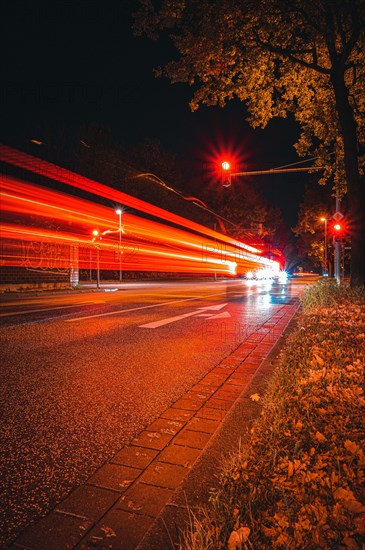 Long exposure of moving cars on a road just in front of an intersection with traffic lights at night with lanterns lit