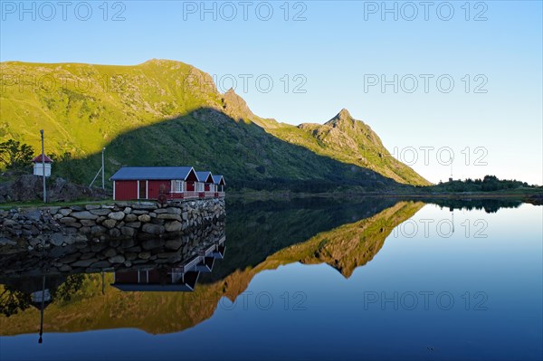 Wooden houses and mountains reflected in the shallow fjord water