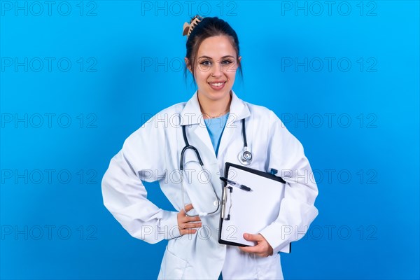 Portrait of smiling female doctor in medical gown standing isolated on blue