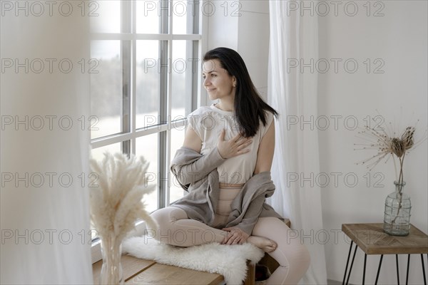 Satisfied woman sits gratefully by the window