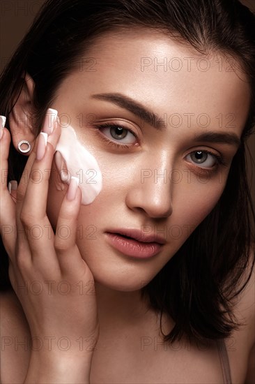 Beautiful young girl with natural nude make-up with cosmetics cream in hands. Beauty face. Photo taken in studio