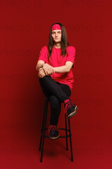 Young man sits on high chair with his leg on his leg