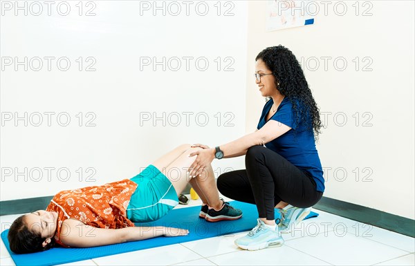 Woman physiotherapist assisting patient lying down doing exercises on the mat