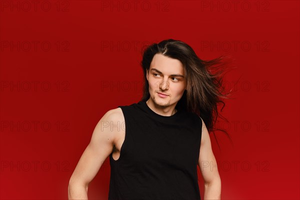 Studio portrait of young handsome man with waiving long hair on red background