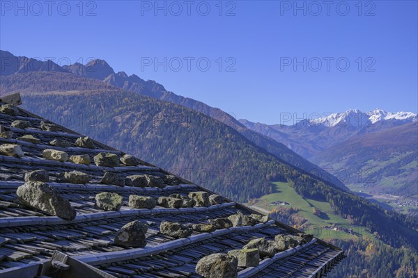 Shingle roof weighted down with stones behind it snow-covered mountains above the Ulten Valley seen from the Pfrollnhof wine tavern