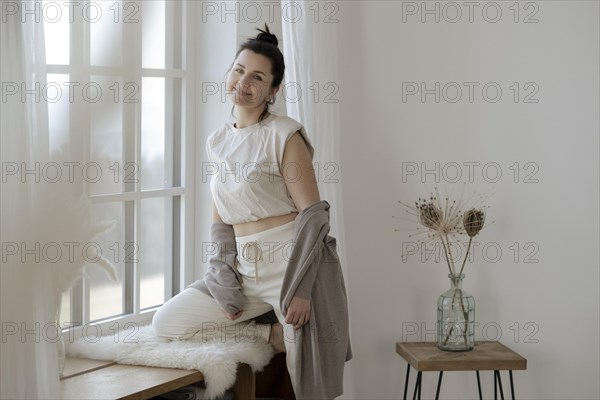 Dark-haired woman sits relaxed at the window