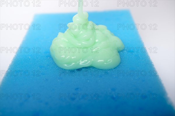 Green liquid soap dripping on a blue sponge on a white background