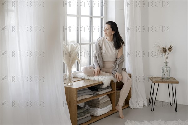 Dark-haired woman sits relaxed at the window