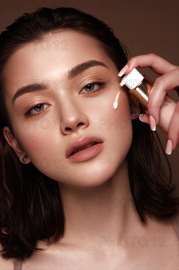 Beautiful young girl with natural nude make-up with cosmetics cream in hands. Beauty face. Photo taken in studio