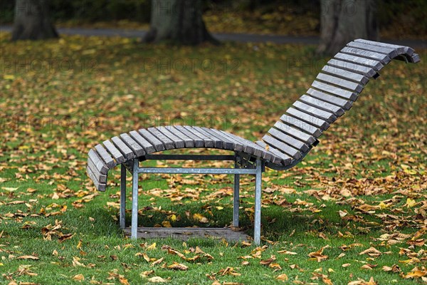 Empty wooden sun lounger in a meadow with autumn leaves