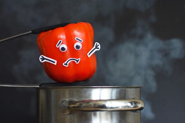 Red Paprika bell pepper with sad face and goggle eyes being put into a steaming cooking pot on dark black background