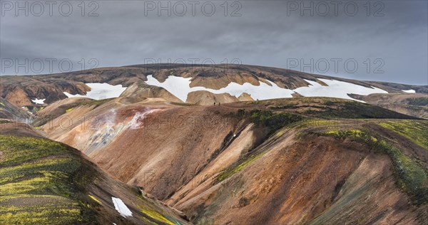 Hikers on colourful rhyolite mountains with remnants of snow