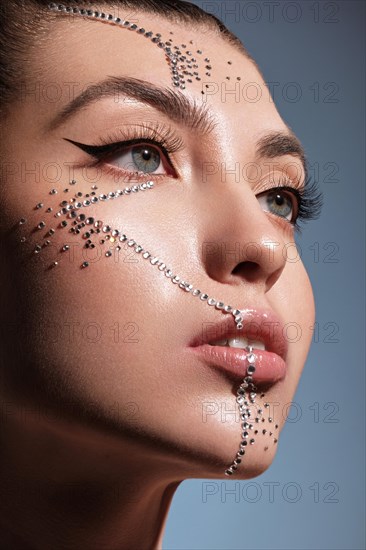 Beautiful woman with creative hairstyle and makeup with rhinestones. Beauty face. Photo taken in the studio