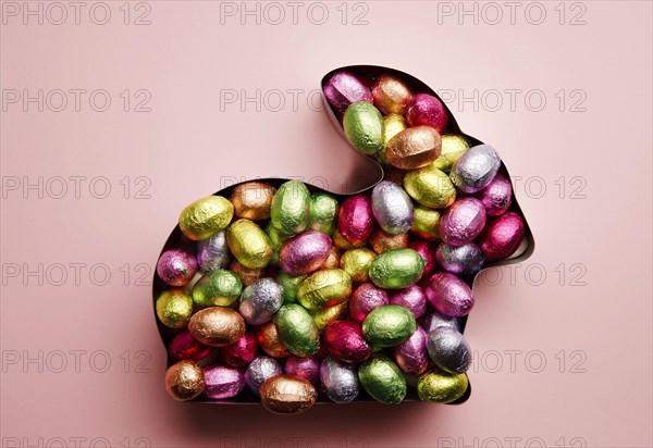 Easter bunny in baking tin filled with chocolate eggs on a salmon background