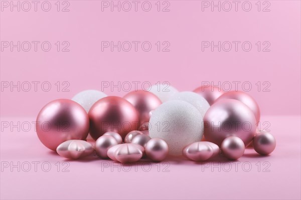 Pile of white and pink Christmas tree ornaments in shape of round ball baubles and stars on pink background