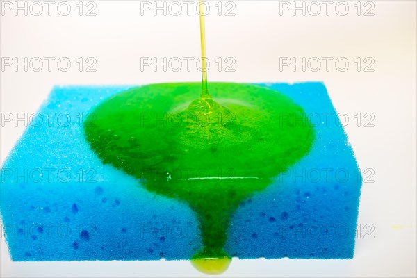 Green liquid soap dripping on a blue sponge on a white background