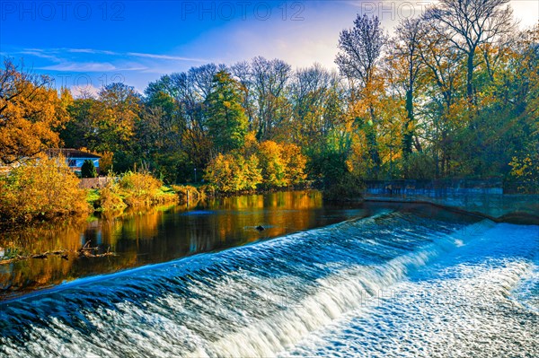 The Leineinsel waterfall next to the Leineinsel residential area in the district of Doehren in autumn with veil clouds