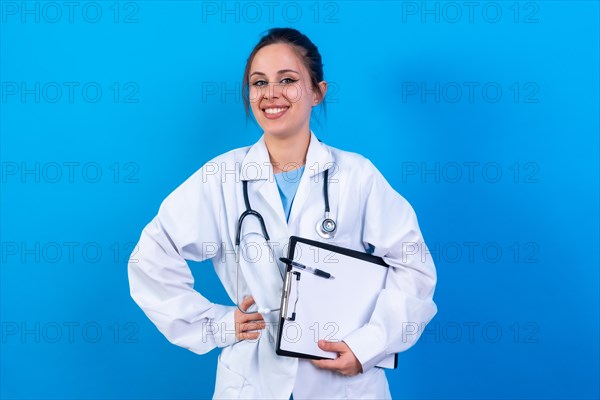 Portrait of smiling female doctor in medical gown standing isolated on blue